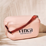 Pink bag with brown strap and 'vinca' branding on a beige background